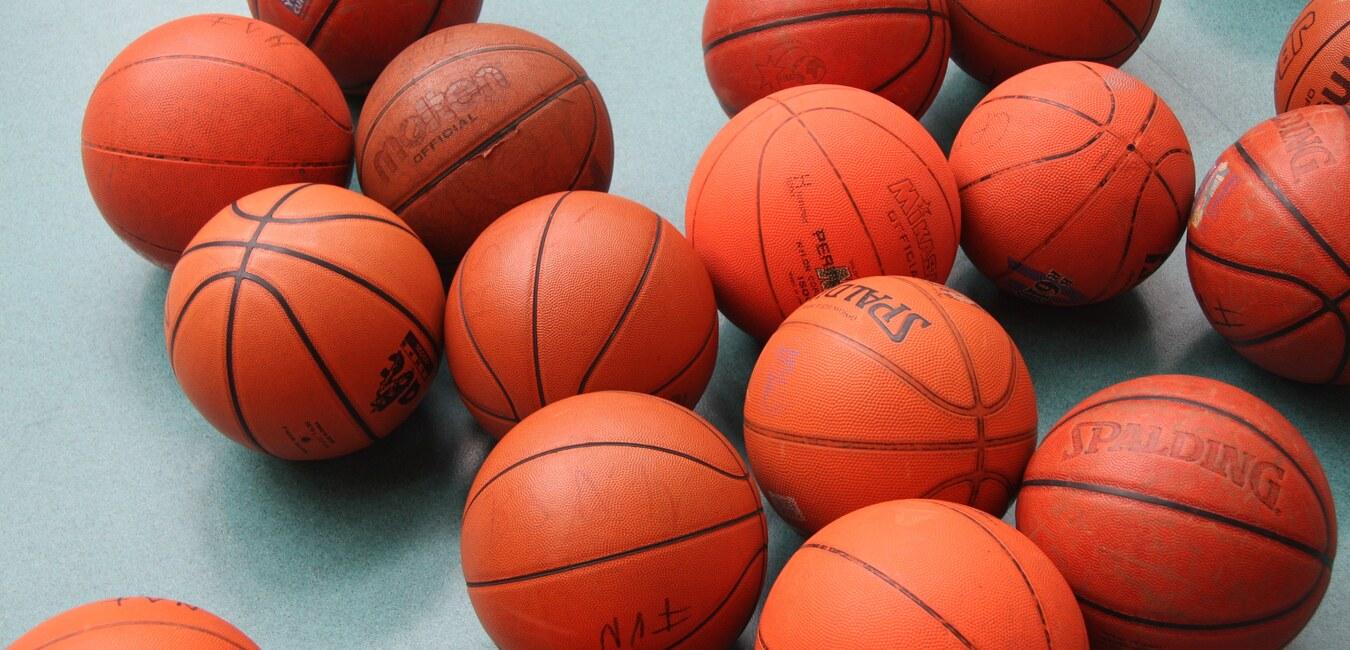 Ansammlung von orangefarbenen Basketballen auf einer grünen Unterlage, verschiedene Marken und Größen sichtbar.